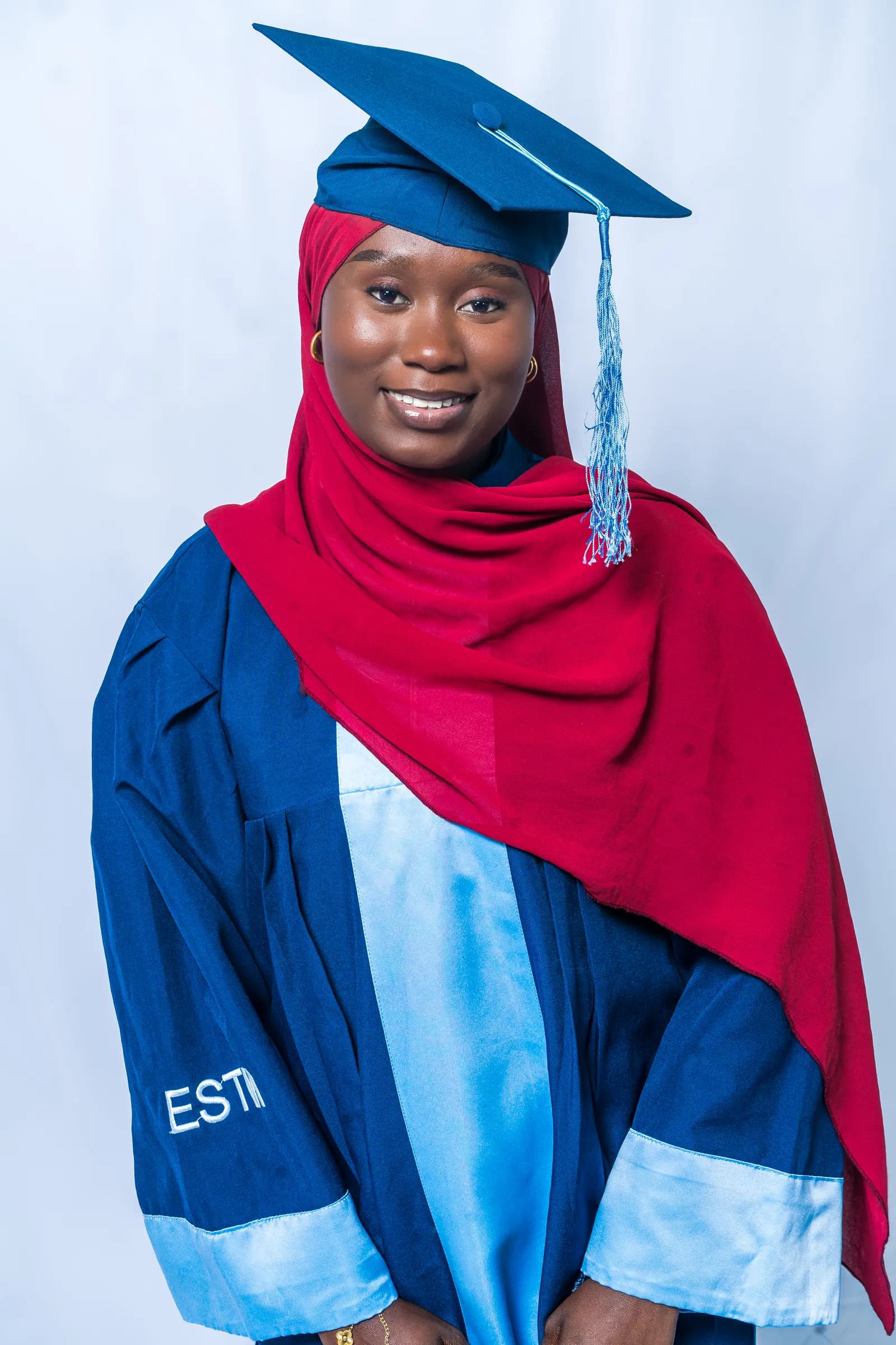 Jeune diplômée de l'ESTM en toge bleue et foulard rouge, souriante.